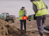 image of researchers in neon vests next to a pile of dirt and a red video play button
