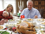 image of family sitting around a table with a variety of good food ready to eat and a red video play button