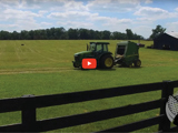 image of farm field with green tractor and black fence and red video play button
