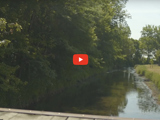 image of water, dock and greenery with red video play button