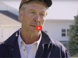 image of farmer with baseball cap, white shirt, black jacket and red video play button