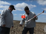image of two men samling soil wearing baseball caps and jackets and a red video play button